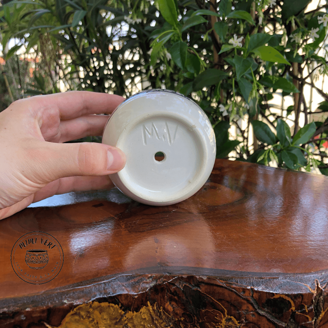 Pot en céramique fait à la main avec des motifs inspirés de l’artisanat marocain, posé sur une table en bois avec des plantes vertes en arrière-plan.