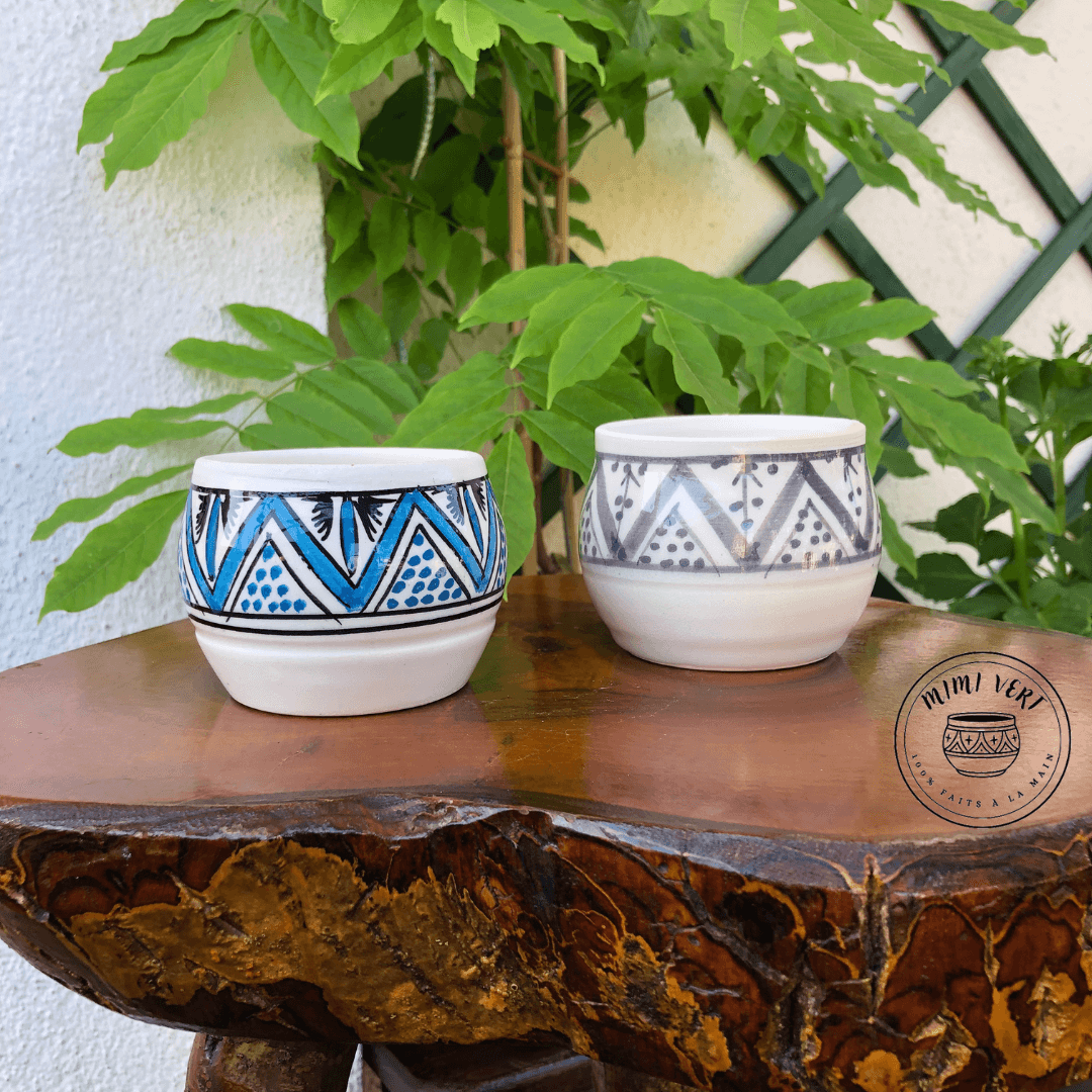 Deux pots en céramique faits à la main avec des motifs inspirés de l’artisanat marocain, posés sur une table en bois avec des plantes vertes en arrière-plan.