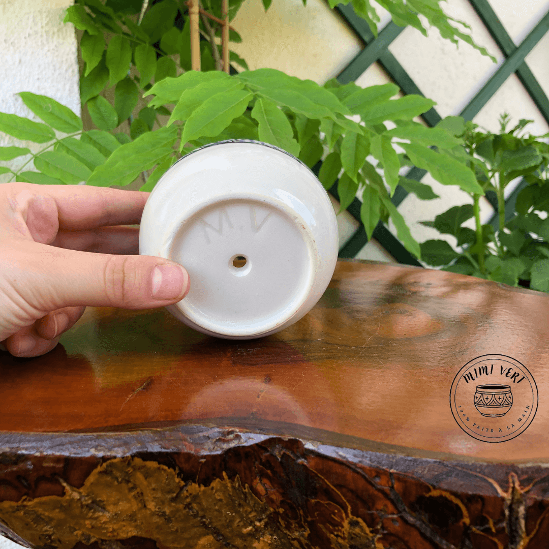 Pot en céramique fait à la main avec des motifs inspirés de l’artisanat marocain, posé sur une table en bois avec des plantes vertes en arrière-plan.