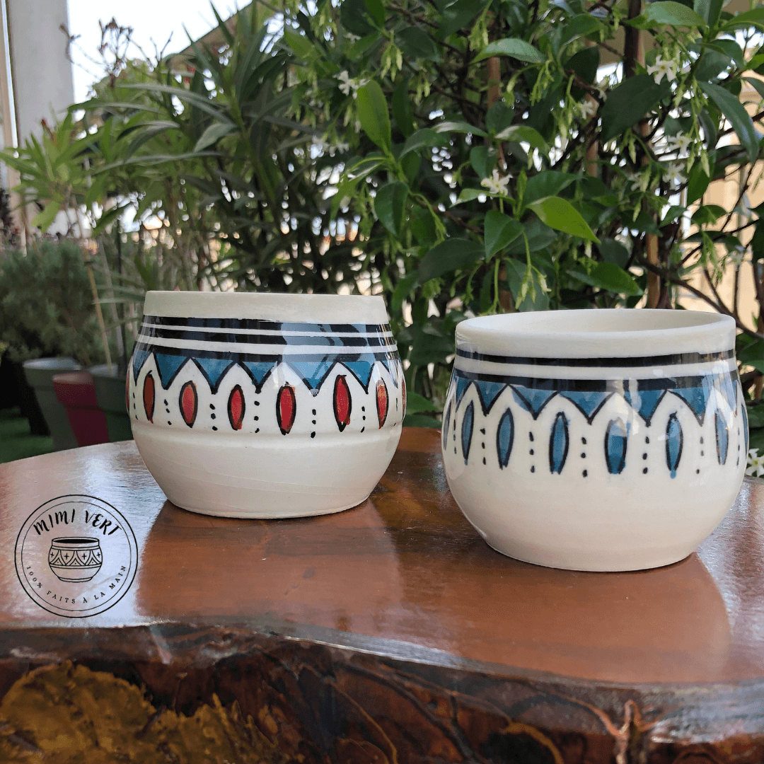 Deux pots en céramique faits à la main avec des motifs inspirés de l’artisanat marocain, posés sur une table en bois avec des plantes vertes en arrière-plan.