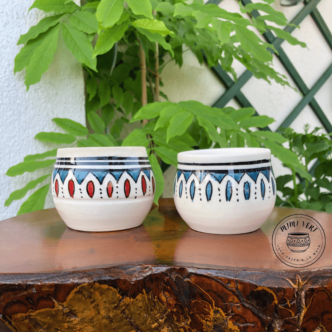 Deux pots en céramique faits à la main avec des motifs inspirés de l’artisanat marocain, posés sur une table en bois avec des plantes vertes en arrière-plan.