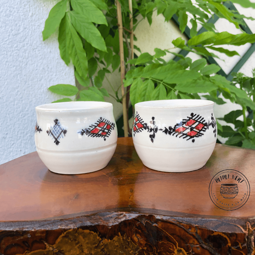Deux pots en céramique faits à la main avec des motifs inspirés de l’artisanat marocain, posés sur une table en bois avec des plantes vertes en arrière-plan.