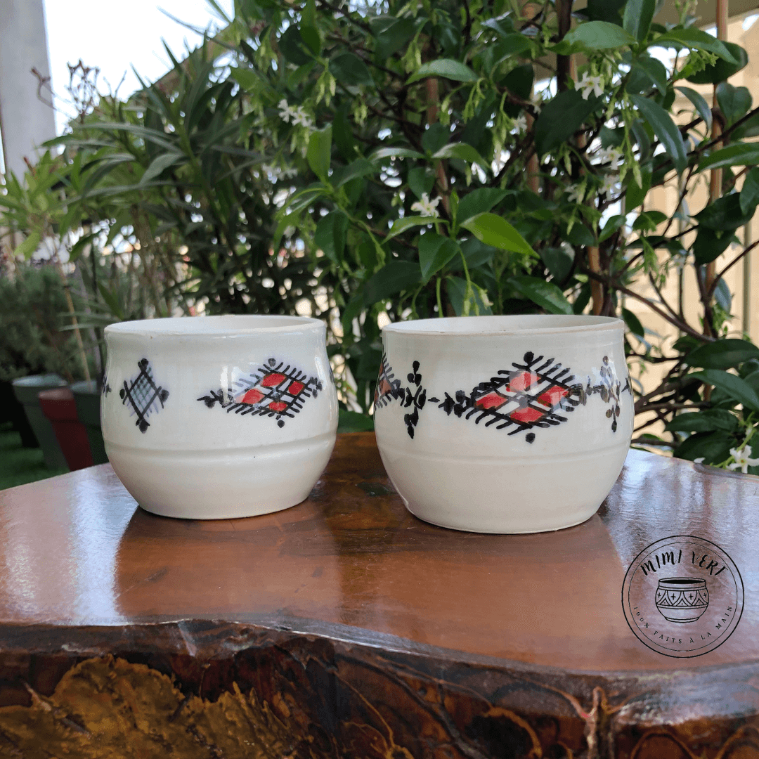 Deux pots en céramique faits à la main avec des motifs inspirés de l’artisanat marocain, posés sur une table en bois avec des plantes vertes en arrière-plan.