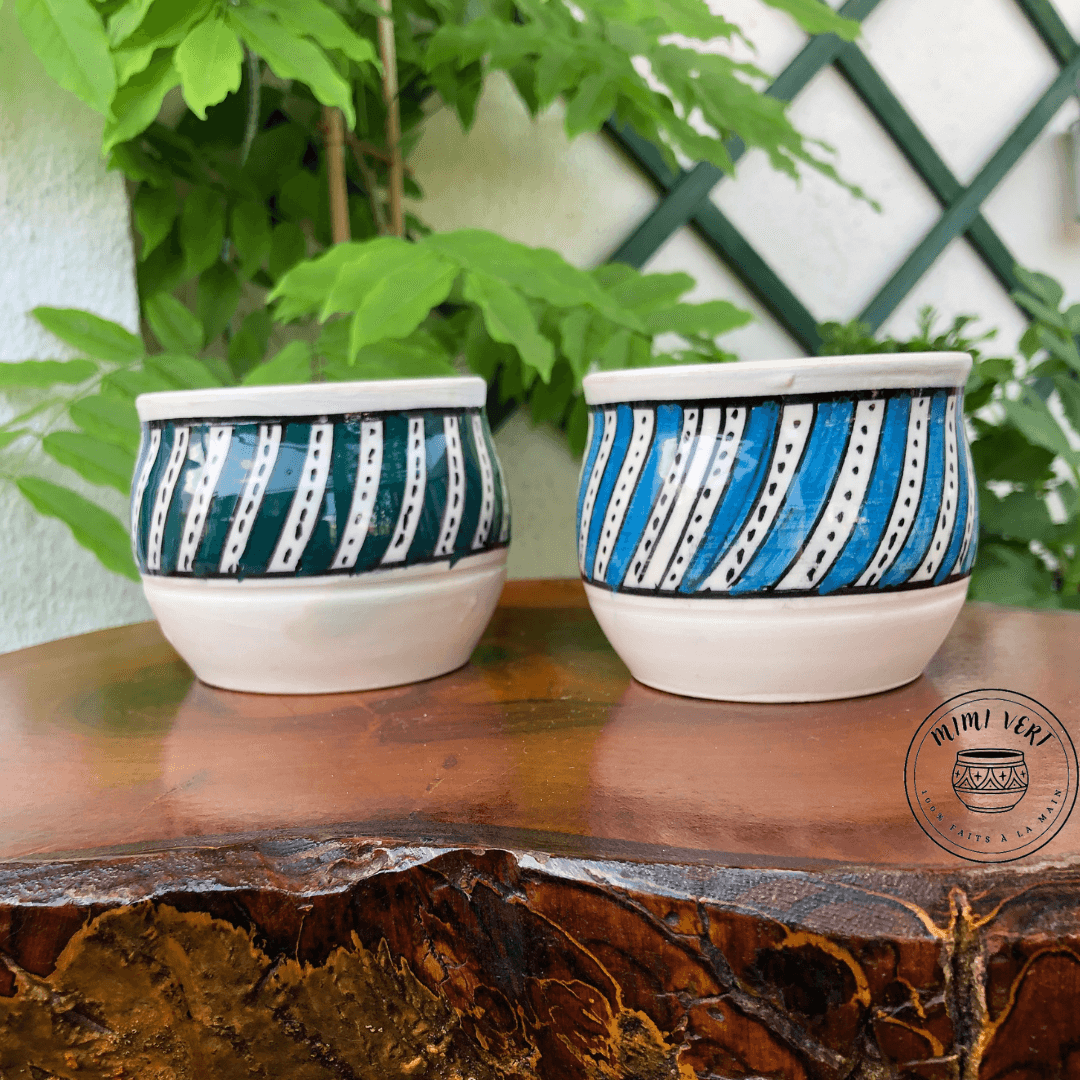 Deux pots en céramique faits à la main avec des motifs inspirés de l’artisanat marocain, posés sur une table en bois avec des plantes vertes en arrière-plan.