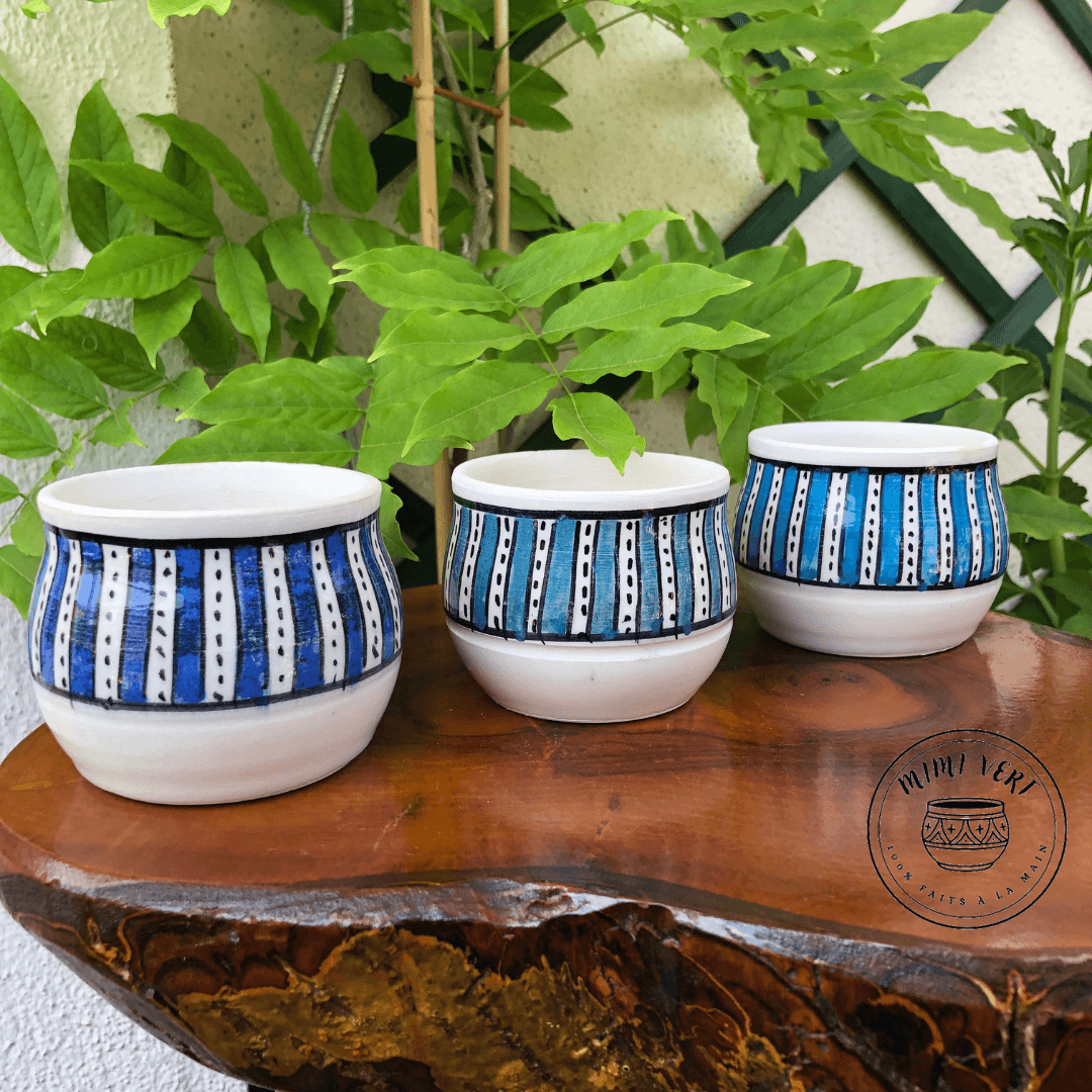 Trois pots en céramique faits à la main avec des motifs inspirés de l’artisanat marocain, sans plantes, posés sur une table en bois avec des plantes vertes en arrière-plan.