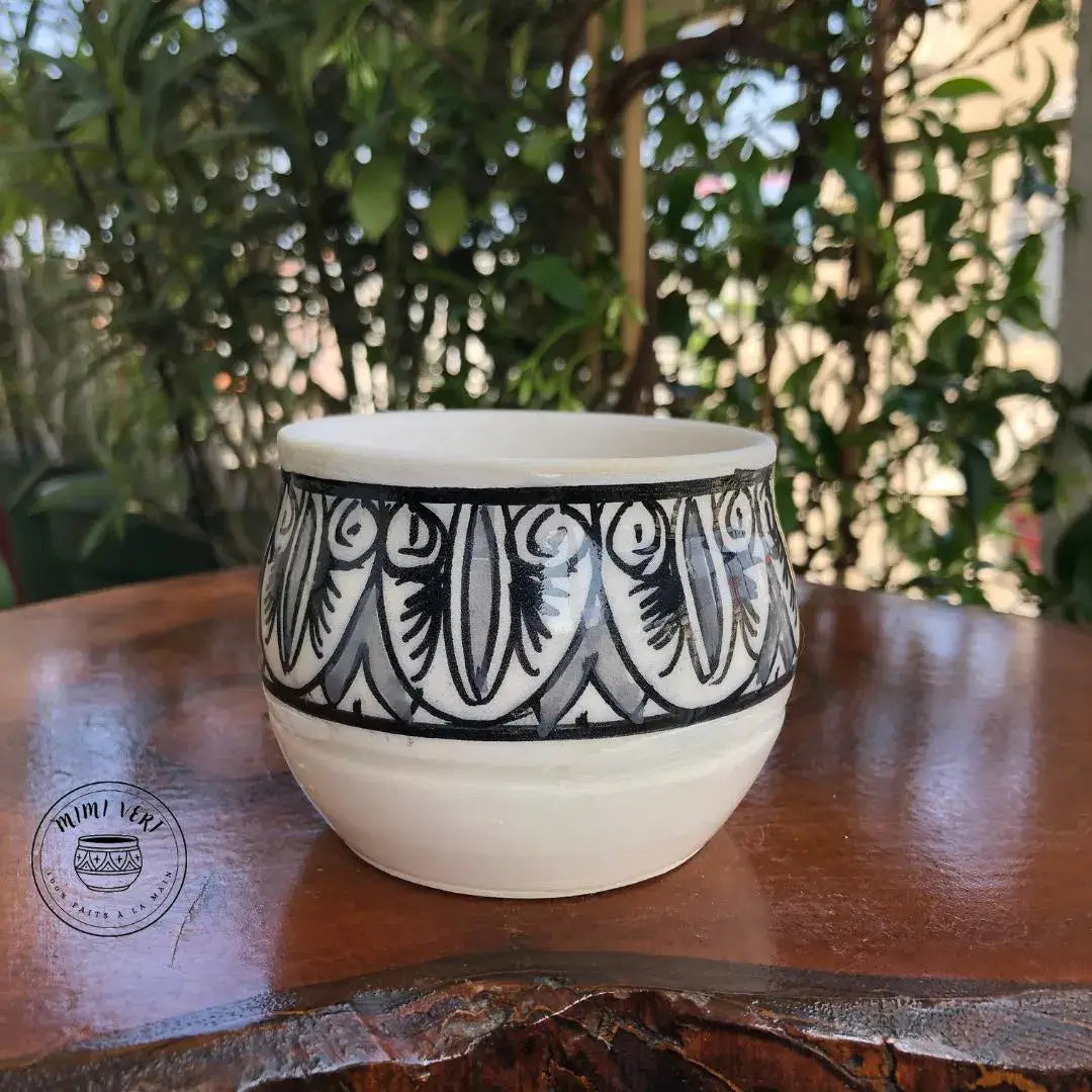 Pot en céramique fait à la main avec des motifs inspirés de l’artisanat marocain, gris noir et blanc, posé sur une table en bois avec des plantes vertes en arrière-plan.
