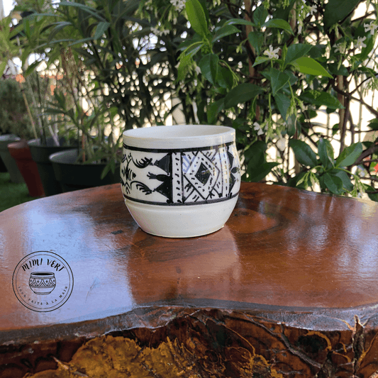 Pot en céramique fait à la main avec des motifs inspirés de l’artisanat marocain, noir et blanc, posé sur une table en bois avec des plantes vertes en arrière-plan.