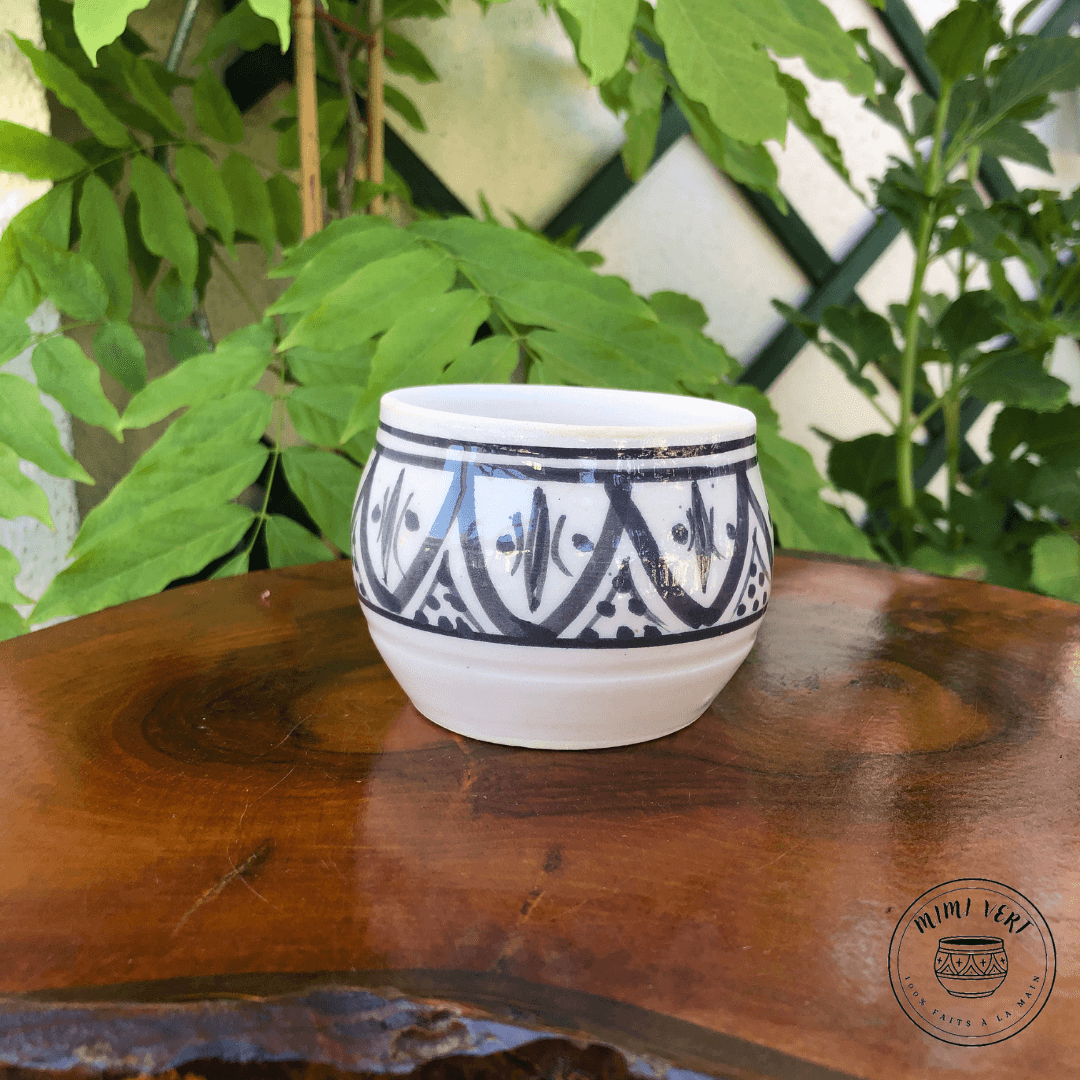 Pot en céramique fait à la main avec des motifs inspirés de l’artisanat marocain, gris et blanc, posé sur une table en bois avec des plantes vertes en arrière-plan.