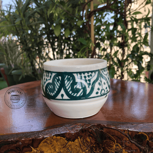 Pot en céramique fait à la main avec des motifs inspirés de l’artisanat marocain, vert et blanc, posé sur une table en bois avec des plantes vertes en arrière-plan.