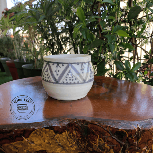 Pot en céramique fait à la main avec des motifs inspirés de l’artisanat marocain gris et blanc, posé sur une table en bois avec des plantes vertes en arrière-plan.